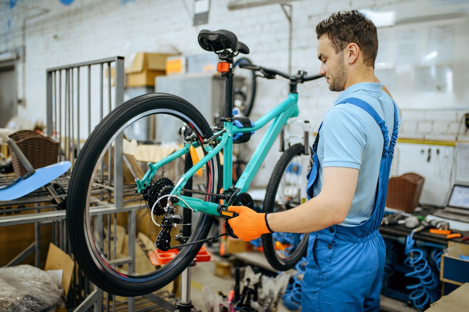 Bicycle factory, worker holds mountain bike. male mechanic in uniform installs cycle parts, assembly line in workshop
