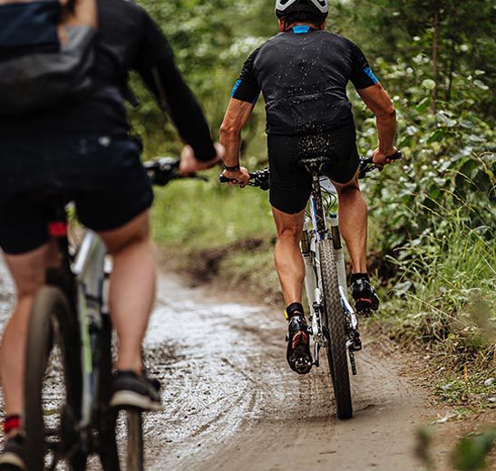 two people riding bikes down a muddy trail